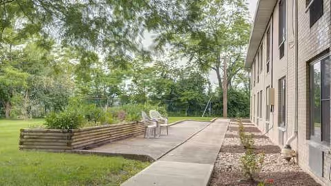 Outdoor walkway along a brick building with a small seating area and greenery.
