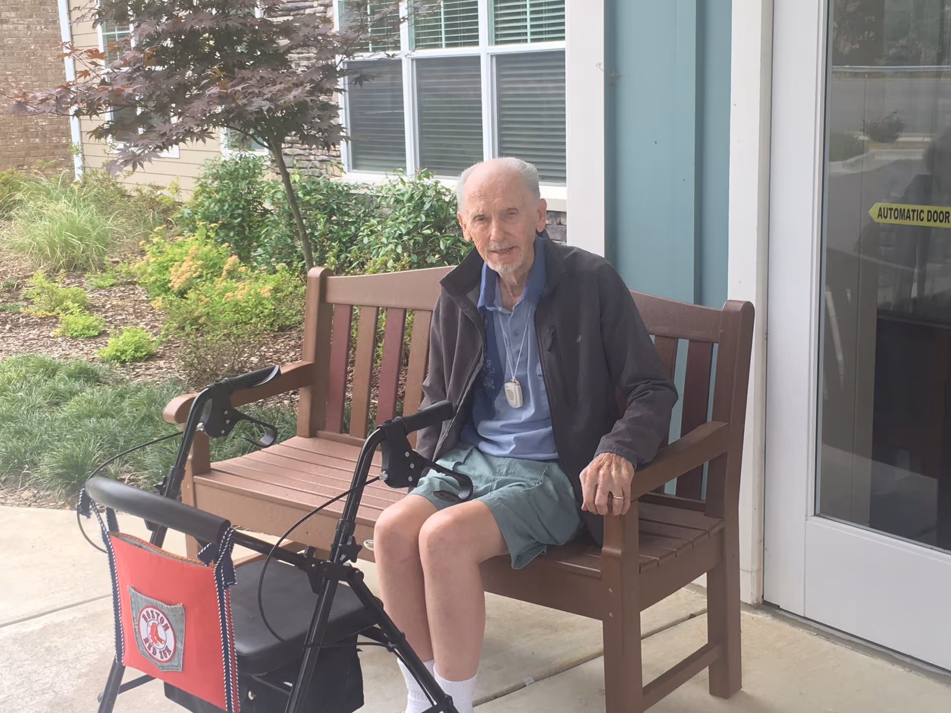 Elderly man seated on a wooden outdoor bench near Thrive at Jones Farm entrance.