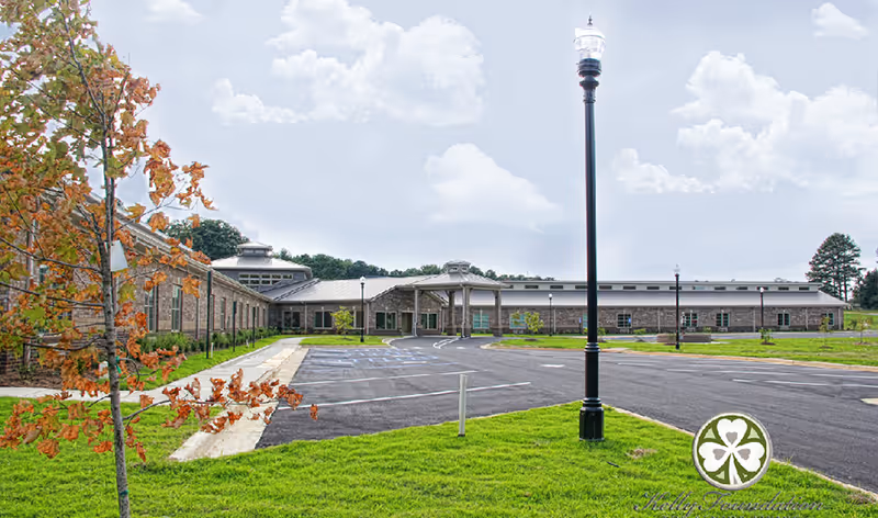 Front exterior view of a single-story senior living building with a circular driveway, lamp posts, and grassy lawn.