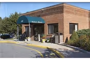 Brick senior living facility entrance with a green awning and surrounding landscaping.