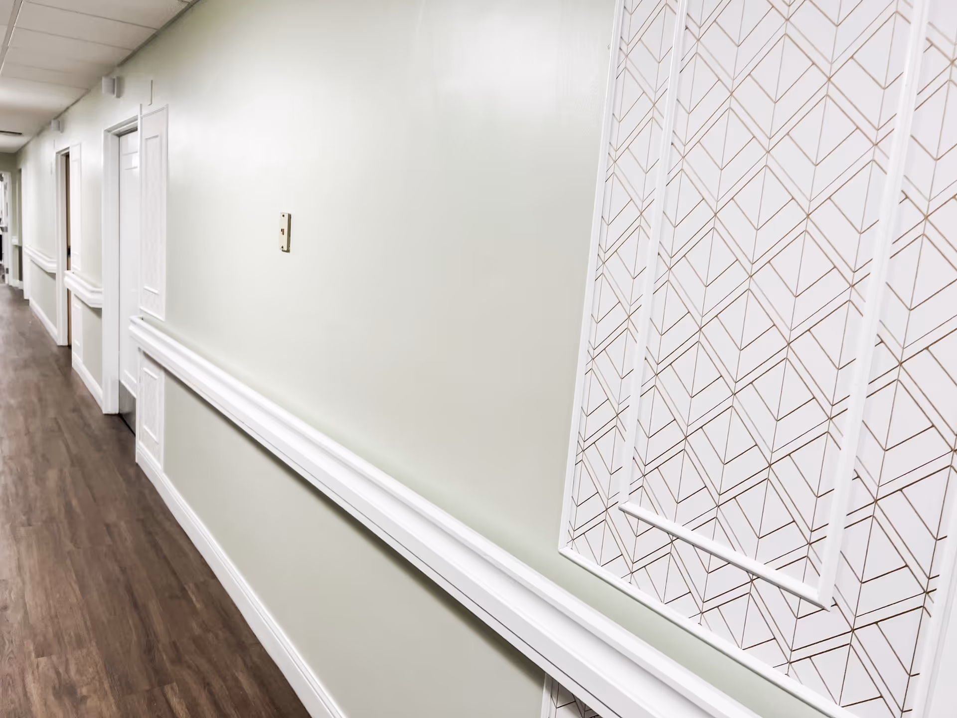 A clean, well-lit interior hallway with wood-look flooring, light green walls, white handrails and decorative wall paneling.