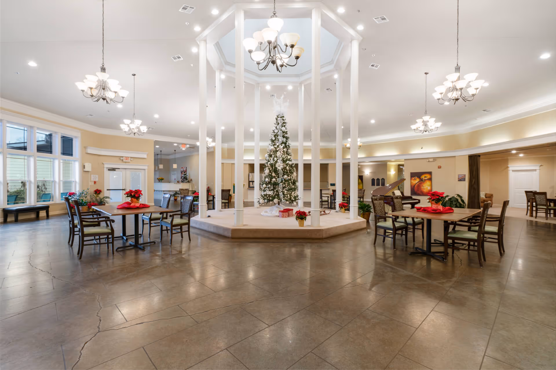 Spacious senior living common dining area with a central decorated Christmas tree, tables and chandeliers.