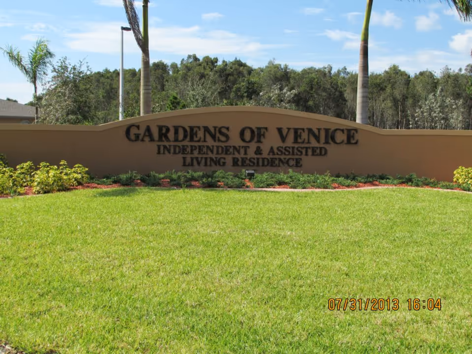 Entrance sign reading 'Gardens of Venice Independent & Assisted Living Residence' set behind a manicured lawn and palm trees.