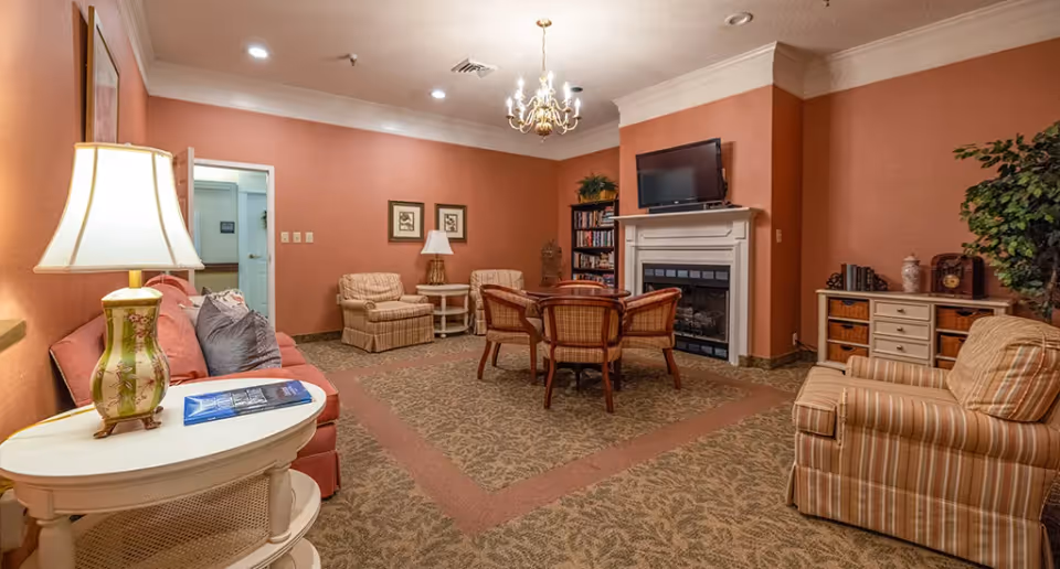 Common sitting room with sofas and armchairs arranged around a table, a fireplace with a TV above, lamps, and warm-colored walls.