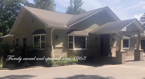 Front exterior of a single-story care facility with a covered entrance and surrounding trees.