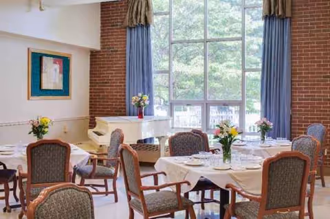 Interior dining room in a senior facility with round tables, chairs, and flowers.