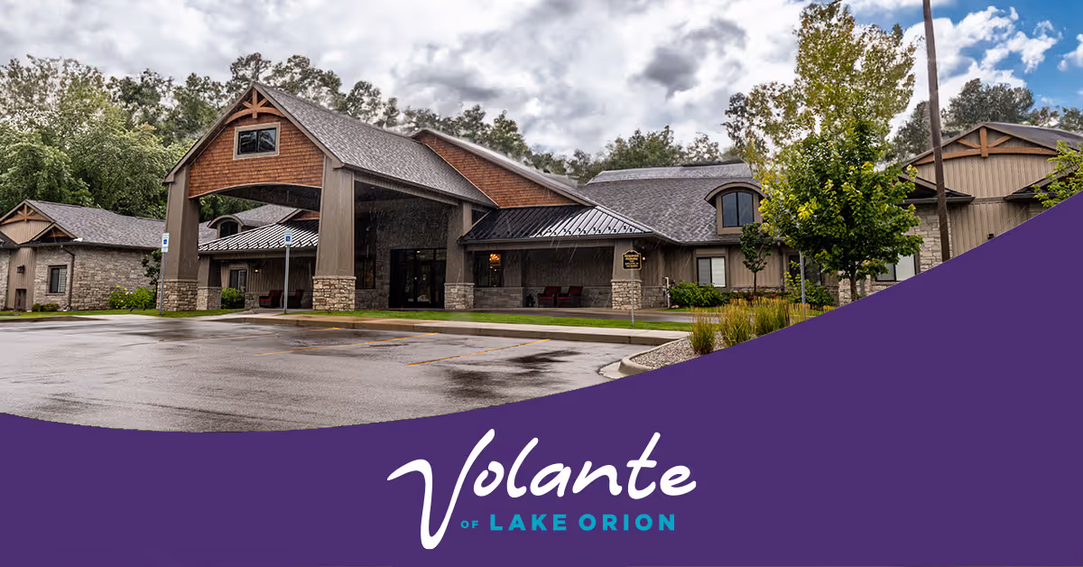 Exterior front of the Volante Senior Living of Lake Orion building with a covered entrance, wet driveway, and a purple branded banner at the bottom.