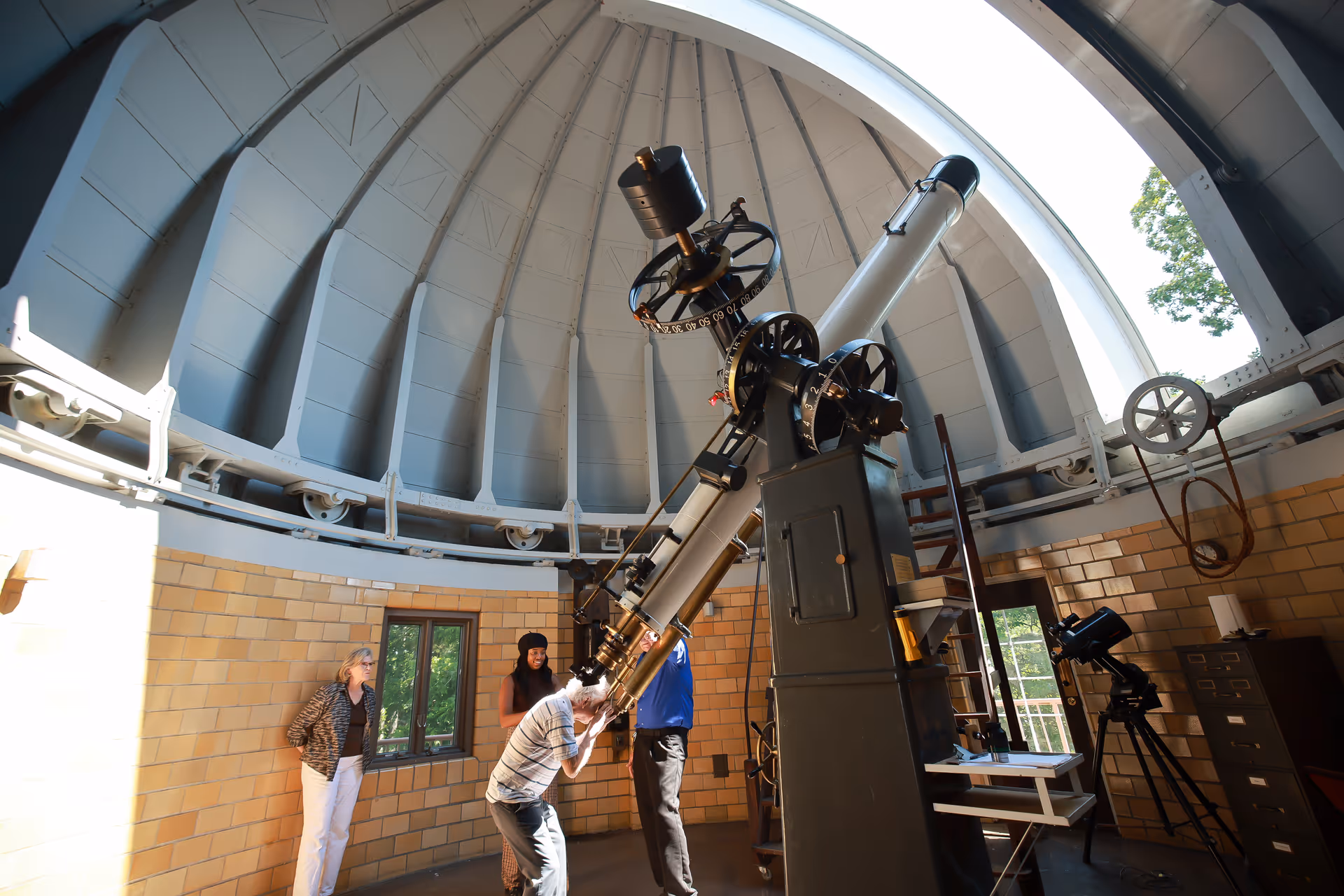 People observing and using a large telescope inside a domed observatory room.