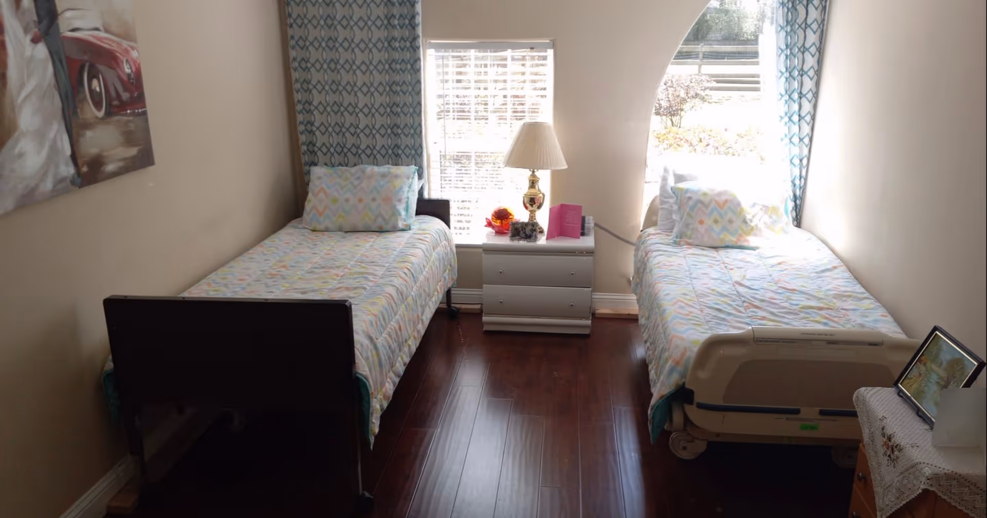 A bright bedroom with two single beds facing a window and a nightstand with a lamp between them.
