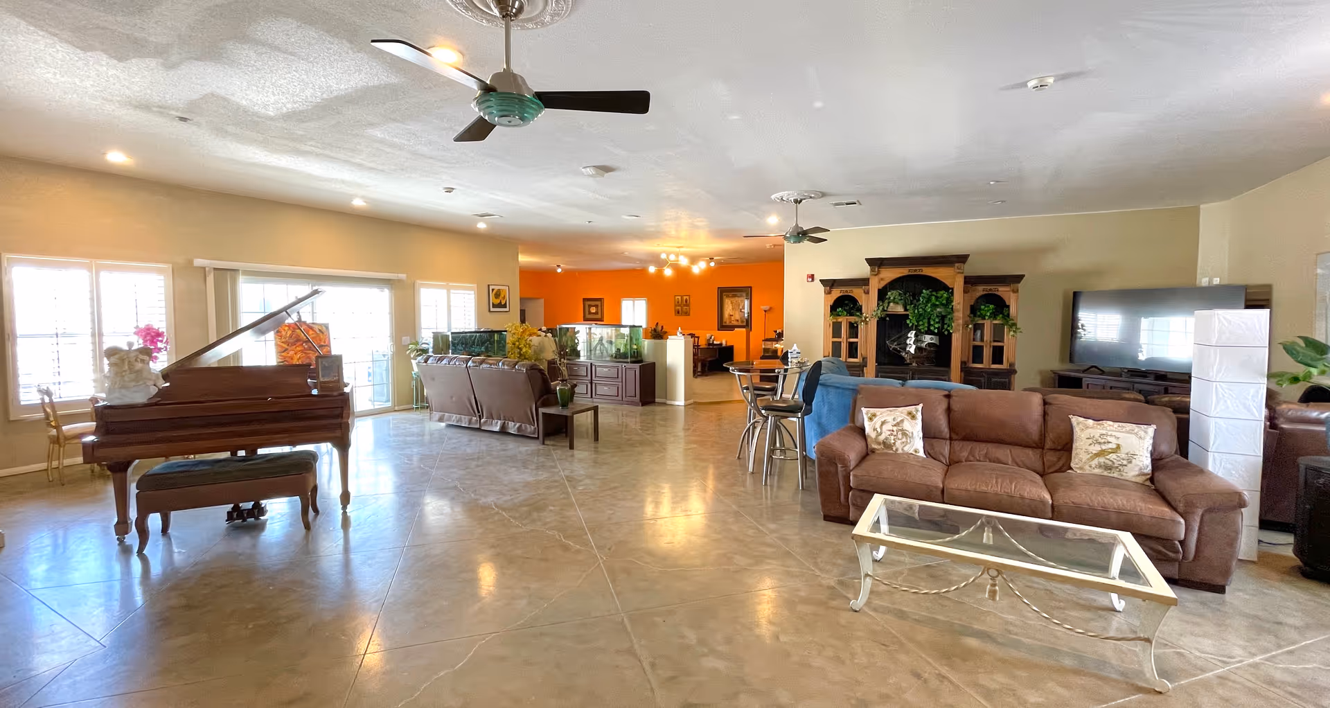 Spacious senior living common room with sofas, a grand piano, TV entertainment center, and seating areas.