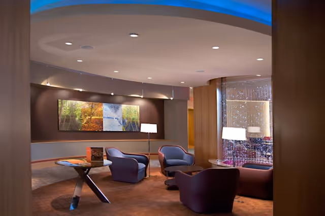 Contemporary seating lounge with several armchairs, small tables, floor lamps, and wall art under curved ceiling lighting.