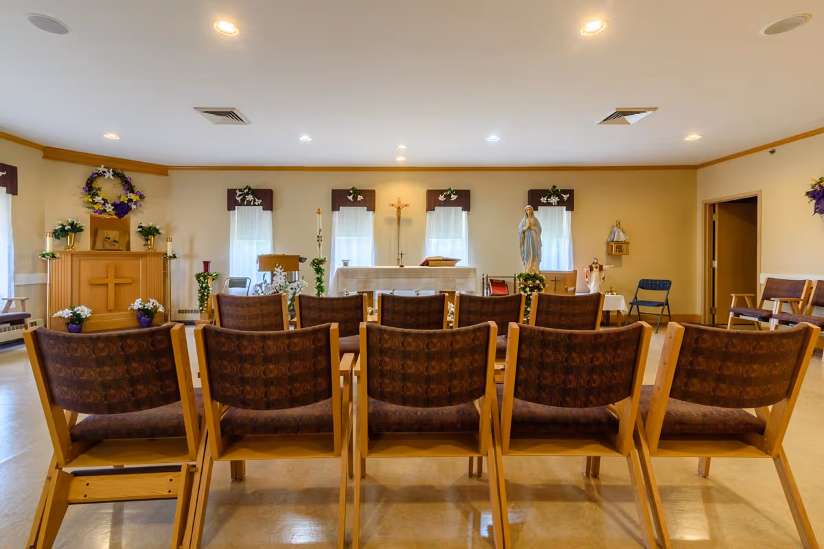 Interior chapel with rows of wooden chairs facing an altar, crucifix, and religious statues.