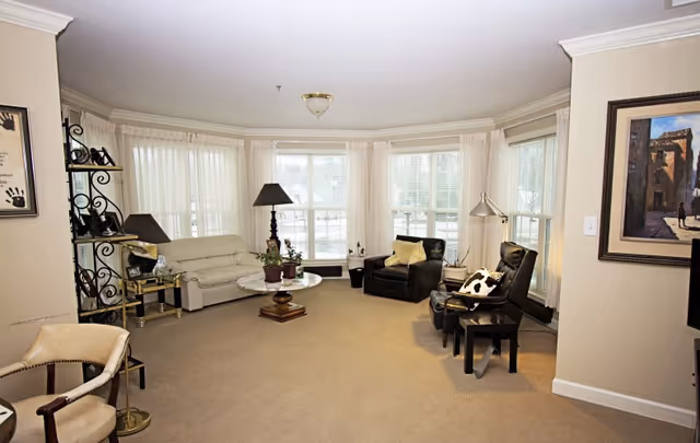 Spacious bright living room with bay windows, a white sofa, black armchairs, coffee tables and lamps.