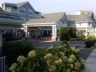 Covered front entrance of a senior living facility with a porte-cochere, landscaped bushes and a driveway.