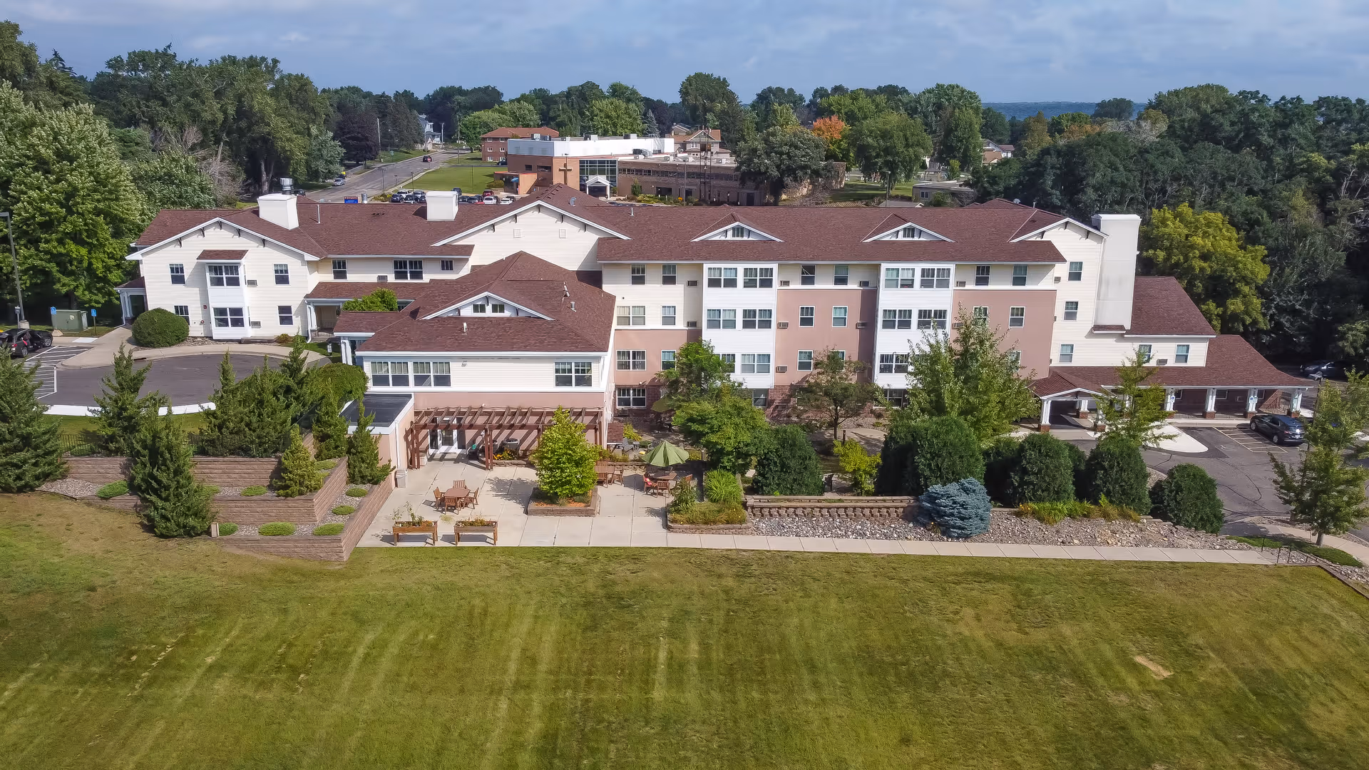 Aerial view of a multi-story senior living building with outdoor patio, landscaped gardens, and a large lawn.