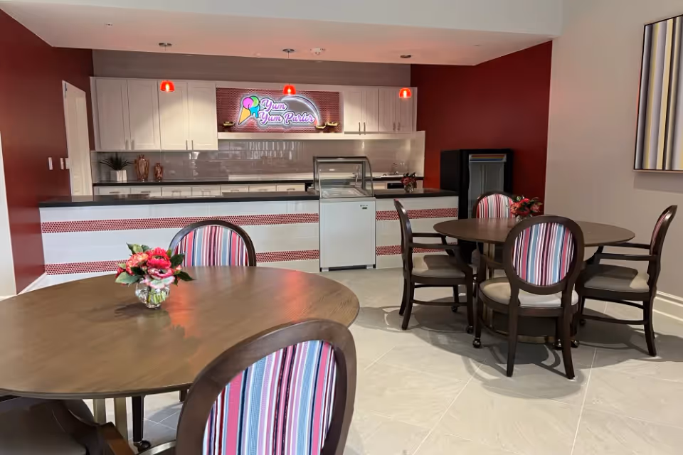 Dining area with round wooden tables and striped chairs facing a serving counter with a 'Yum Yum Parlor' sign.