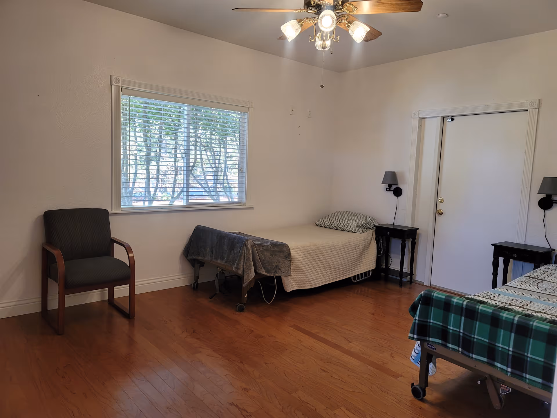 Simple bedroom with two single beds, a chair, nightstands, a window with blinds, and a ceiling fan.