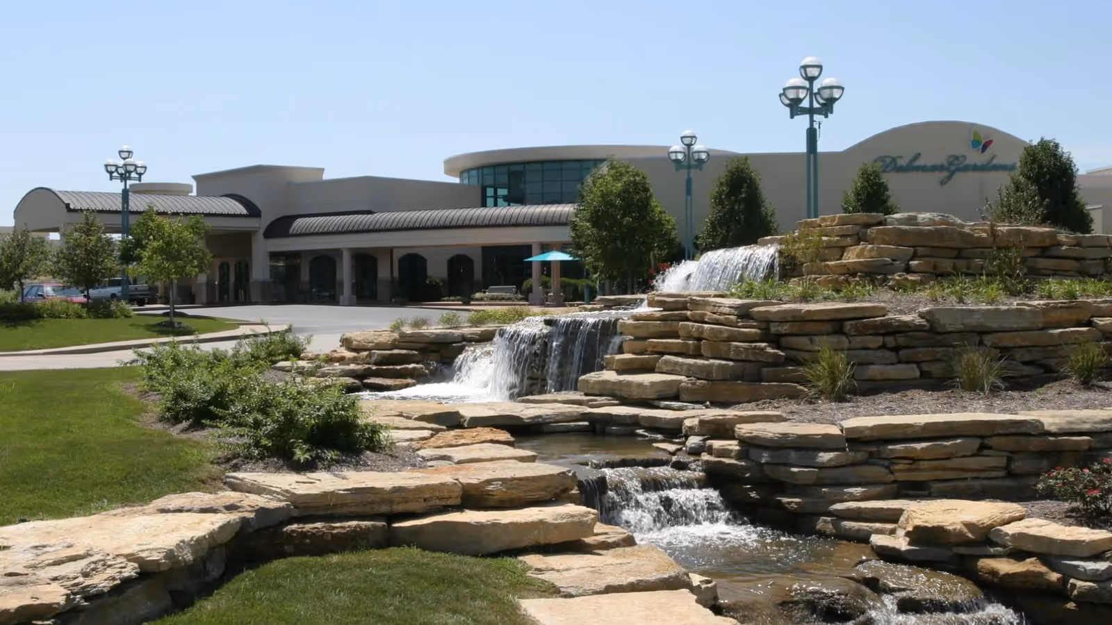 Entrance of a senior living facility with a tiered rock waterfall and landscaped lawn in front of the building.