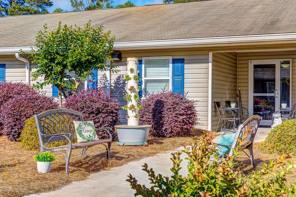 A small courtyard with benches, potted plants, and shrubs in front of a single-story building.