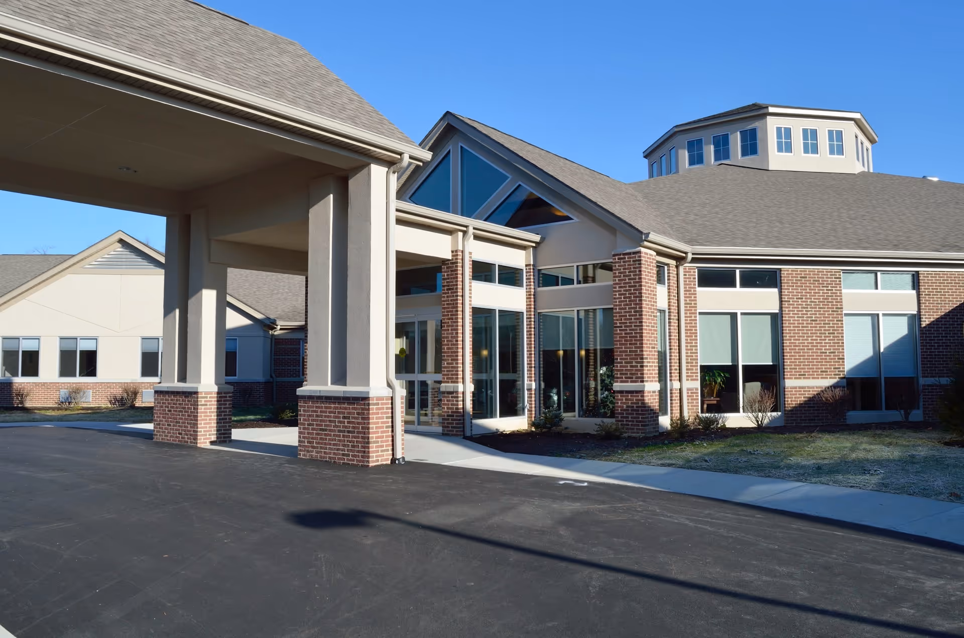 Front entrance of a brick and stucco senior living building with a covered porte-cochère and large windows.