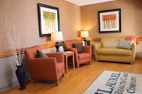 Cozy lounge area with red chairs, a beige sofa, lamps, and framed artwork.