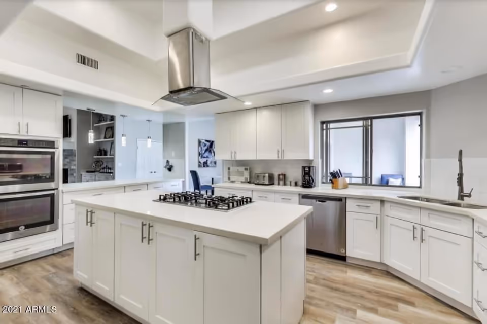 Spacious bright kitchen with a large center island featuring a gas cooktop, white cabinets, and stainless steel appliances.