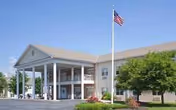 Front view of Complete Care at Berkshire, a senior living facility with pillars and American flag.