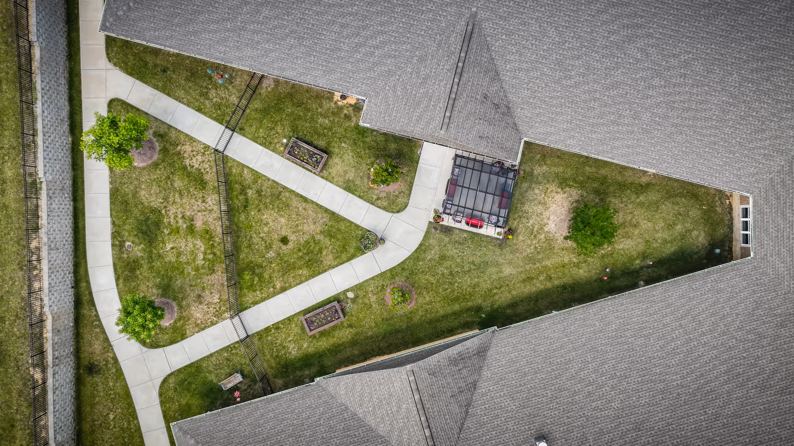 Aerial view of a triangular courtyard with intersecting concrete walkways, grassy lawns, planter boxes and surrounding building roofs.