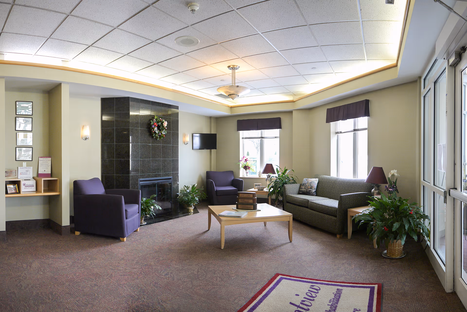 Bright senior living lounge with a sofa, armchairs, coffee table, fireplace and potted plants.
