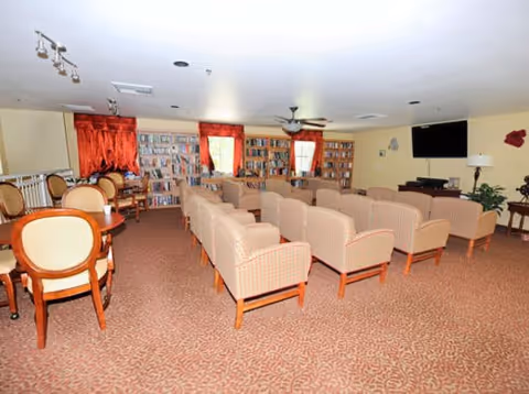 A large communal sitting and library area with rows of upholstered armchairs, tables, bookshelves and a wall-mounted TV.
