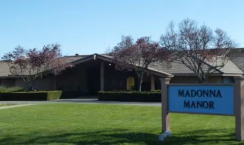 Exterior view of Madonna Gardens sign with the building and lawn in the background.