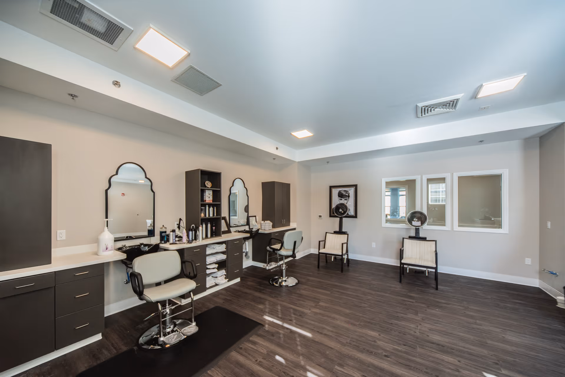 Salon-style interior with styling chairs, mirrors, cabinets, and two hooded hair dryers.