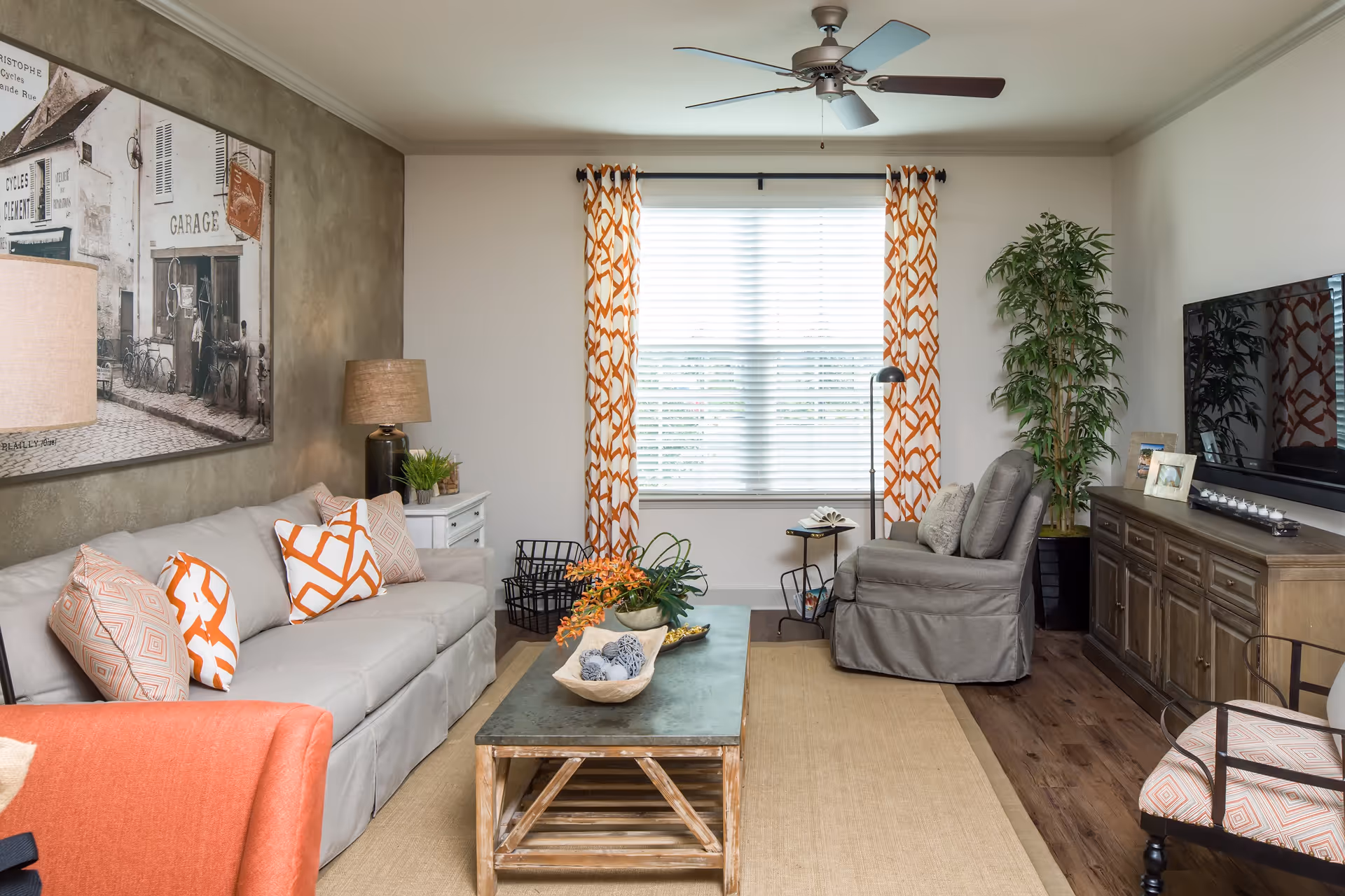 Bright living room with a sofa, armchair, coffee table, TV console, and a window with patterned curtains.