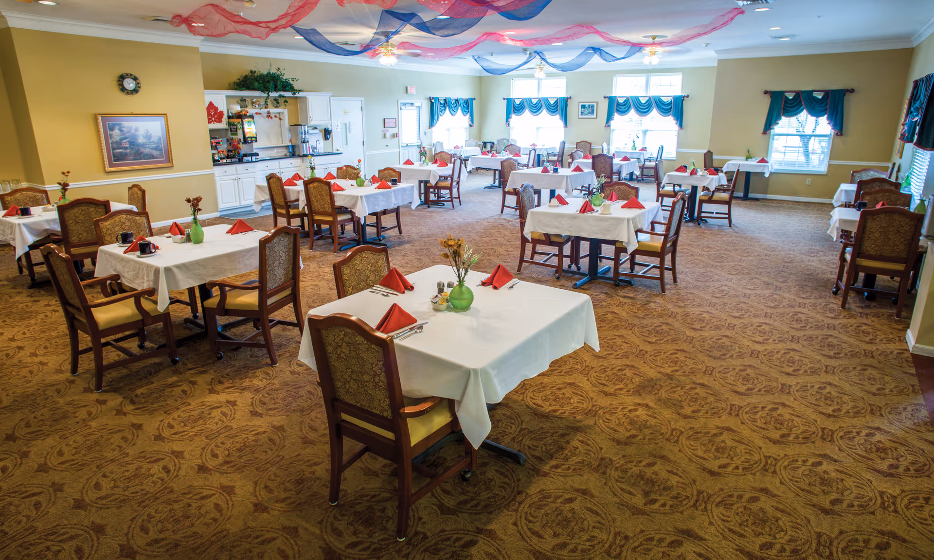 Large dining room with many tables covered in white tablecloths, red napkins, and chairs arranged throughout.