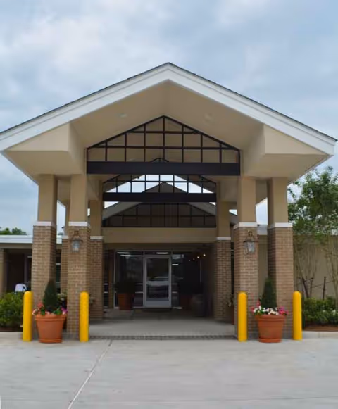 Front entrance of Zachary Manor Nursing and Rehabilitation Center with pillars, glass doors, and planters.
