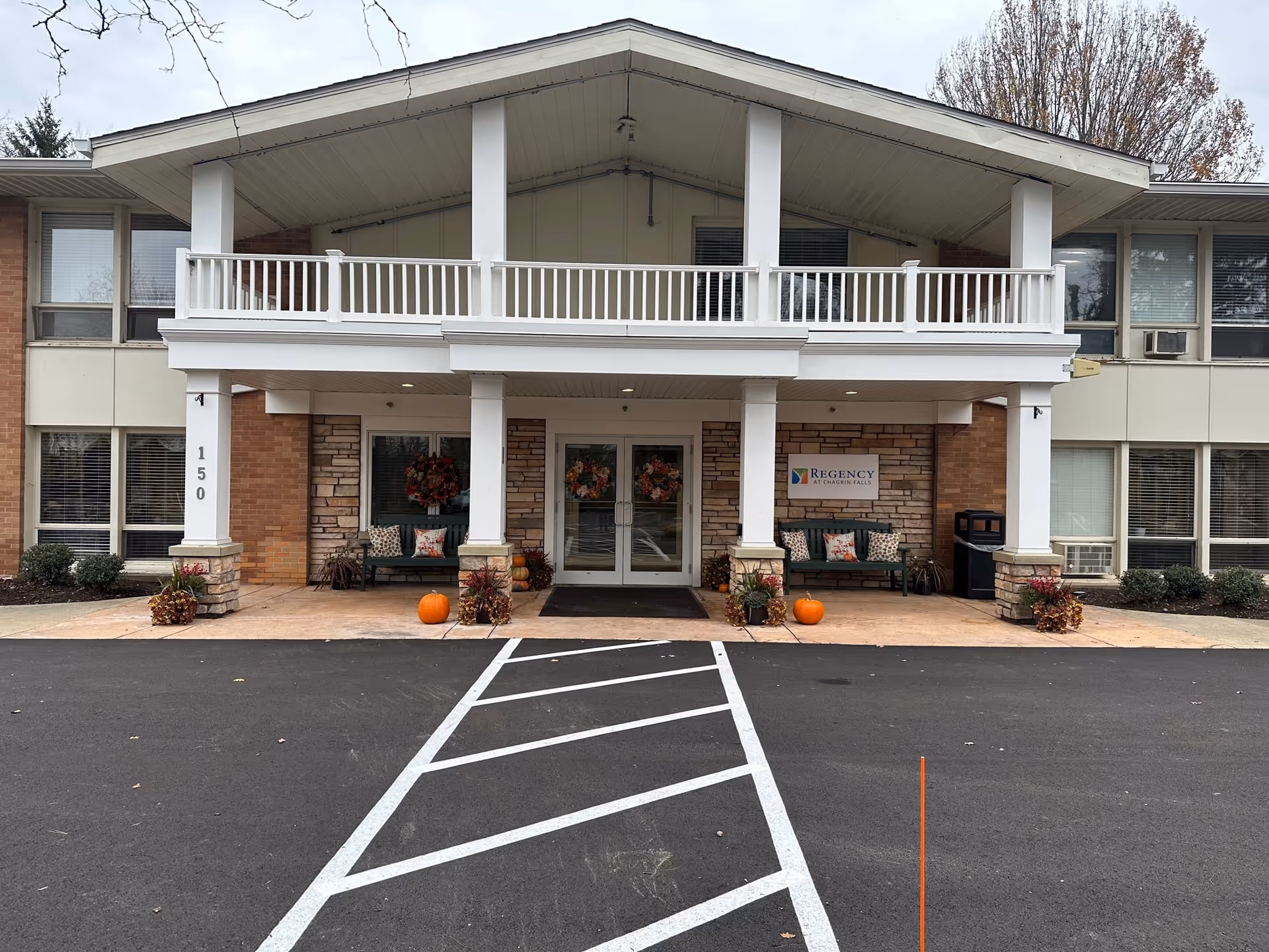Front entrance of the Regency at Chagrin Falls building with a covered two-story portico, seating, seasonal wreaths and pumpkins.
