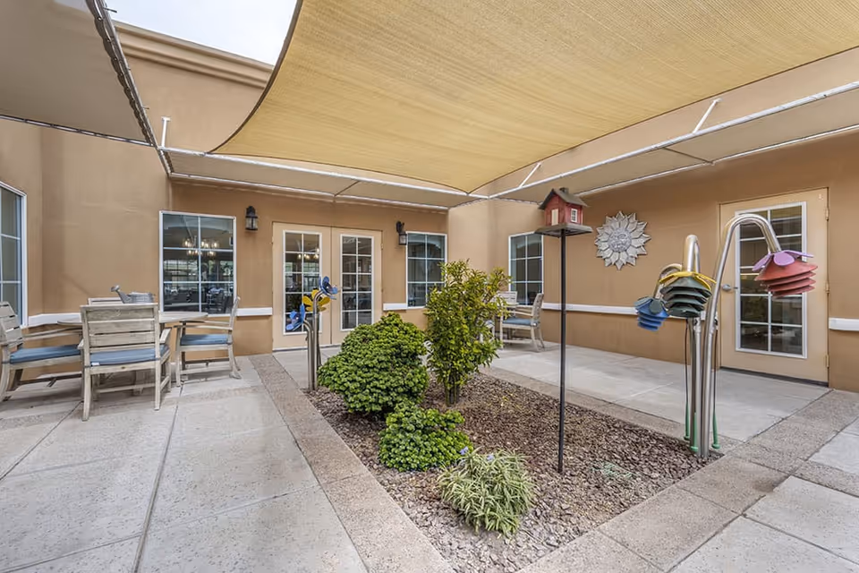 Shaded courtyard patio with tables, chairs, raised planters, and decorative birdhouses outside the building.