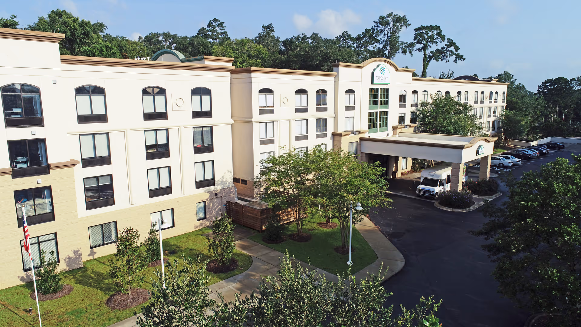 Front exterior of a multi-story senior living building with a covered entrance, parking lot and landscaped grounds.