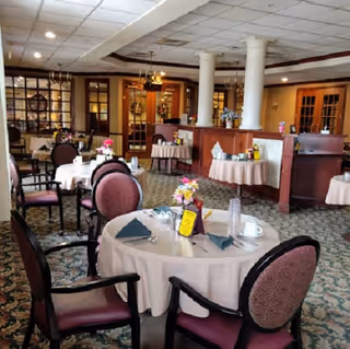 Interior dining room with round tables, pink chairs, floral centerpieces, and a service area in back.