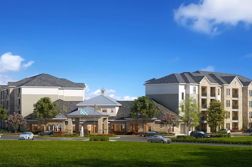 Exterior view of The Retreat at Barber's Hill, showing a large senior living facility with multiple stories, stone and siding facade, several trees, parked cars, and a clear blue sky.
