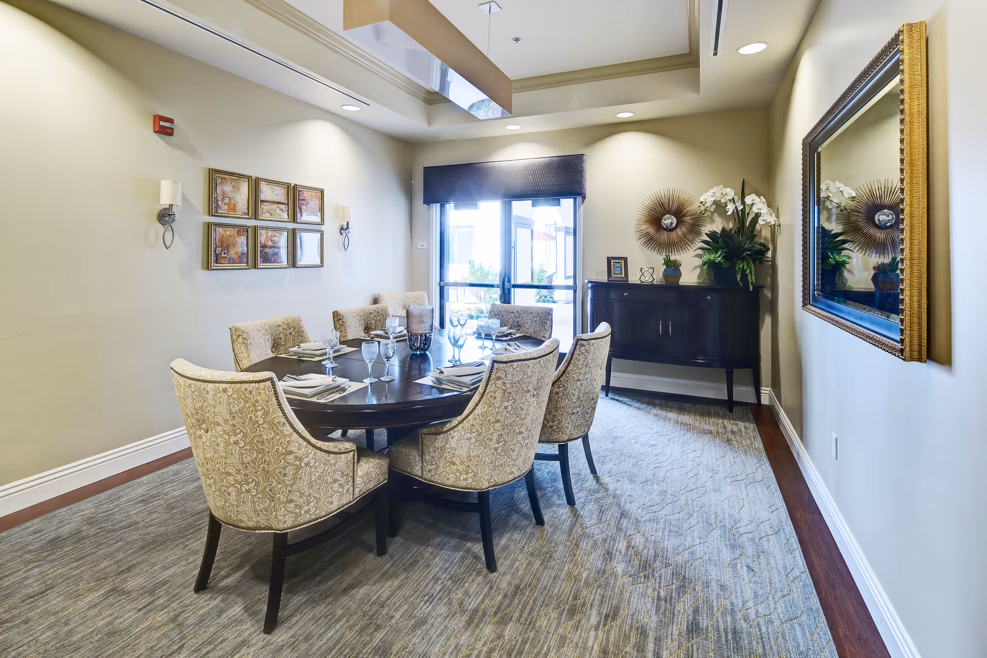 Well-appointed dining room with a round table set for guests, upholstered chairs, sideboard, wall art, and a large mirror.