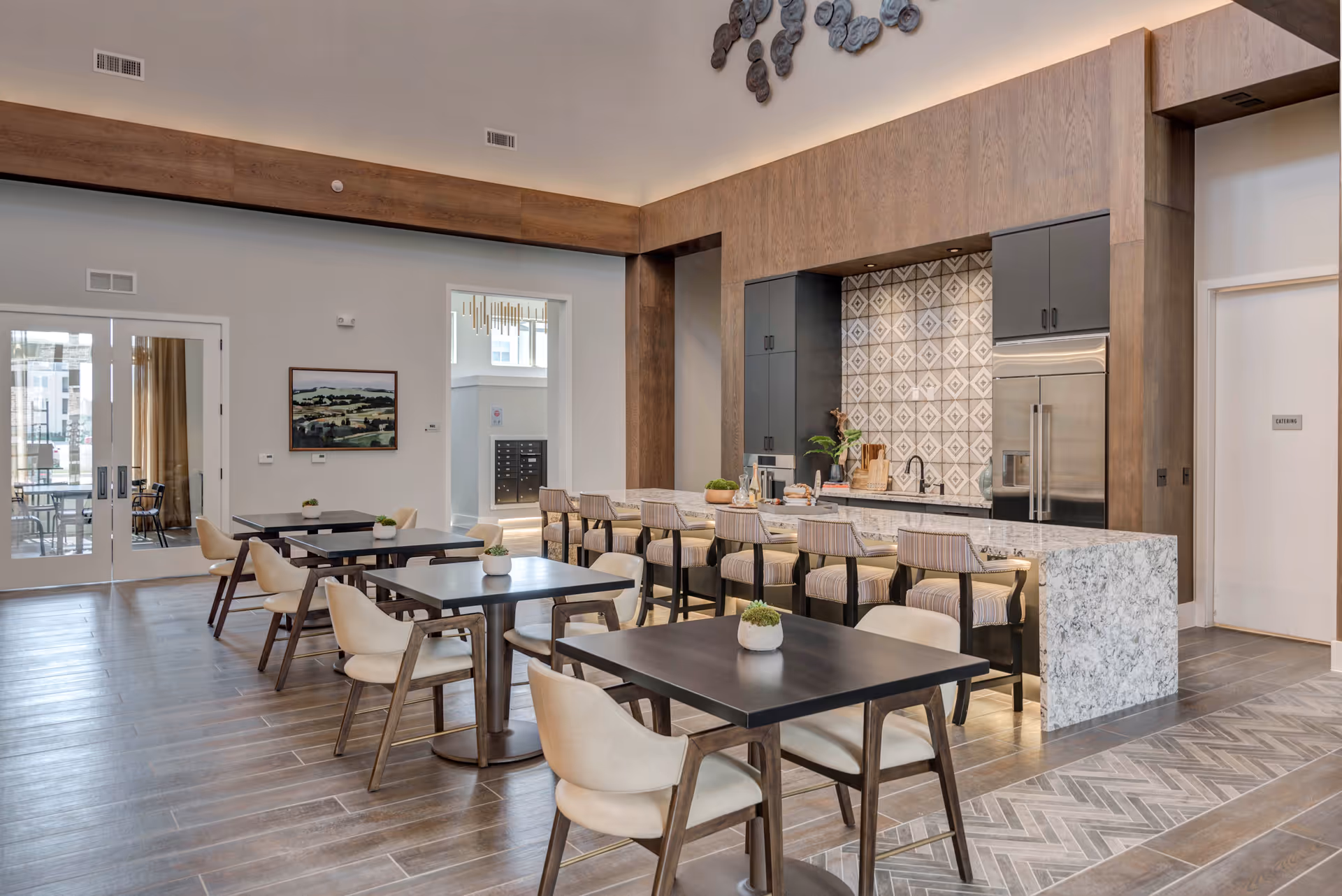 Spacious communal dining area with multiple tables and chairs and a marble-topped kitchen island with barstools under high ceilings.