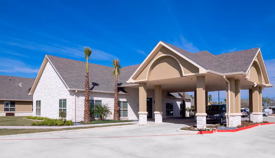 Exterior view of Mid Valley Nursing & Rehabilitation building with a covered entrance supported by columns, palm trees, and a clear blue sky.