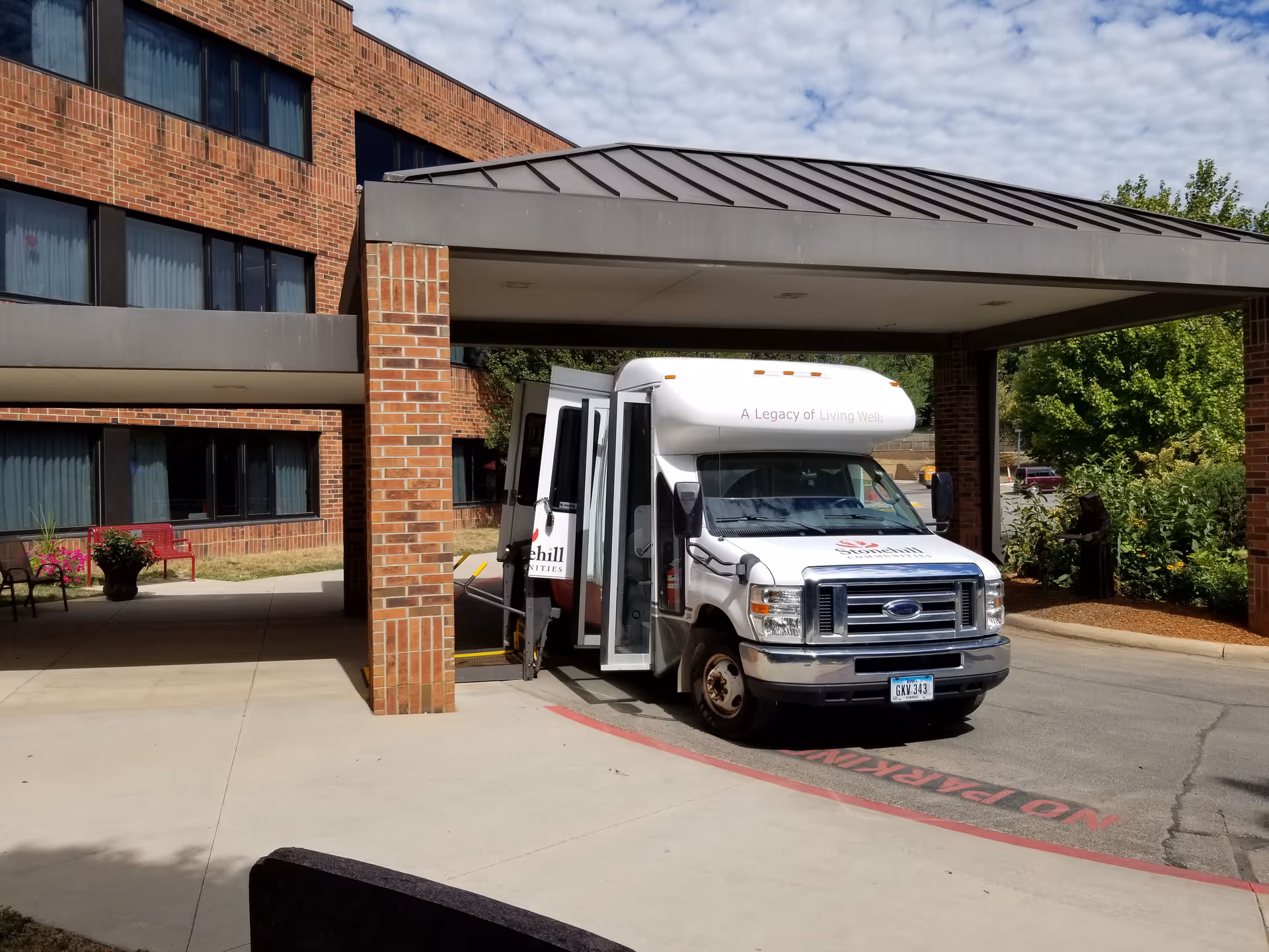 A white shuttle van parked under the covered entrance of a brick senior living facility.