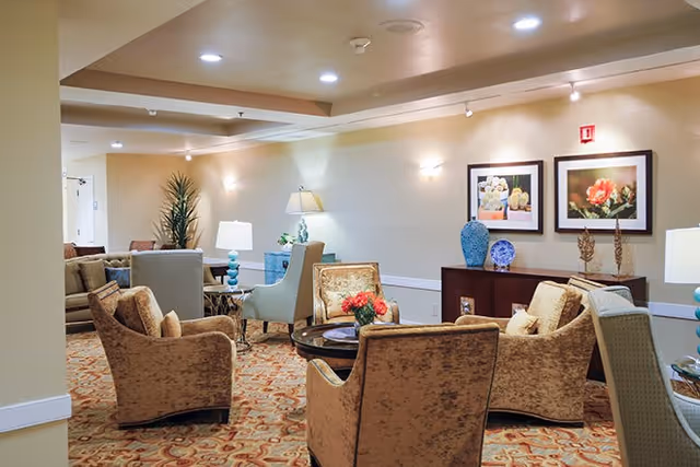 Cozy communal lounge with upholstered armchairs arranged around a coffee table, lamps, framed artwork, and decorative vases.