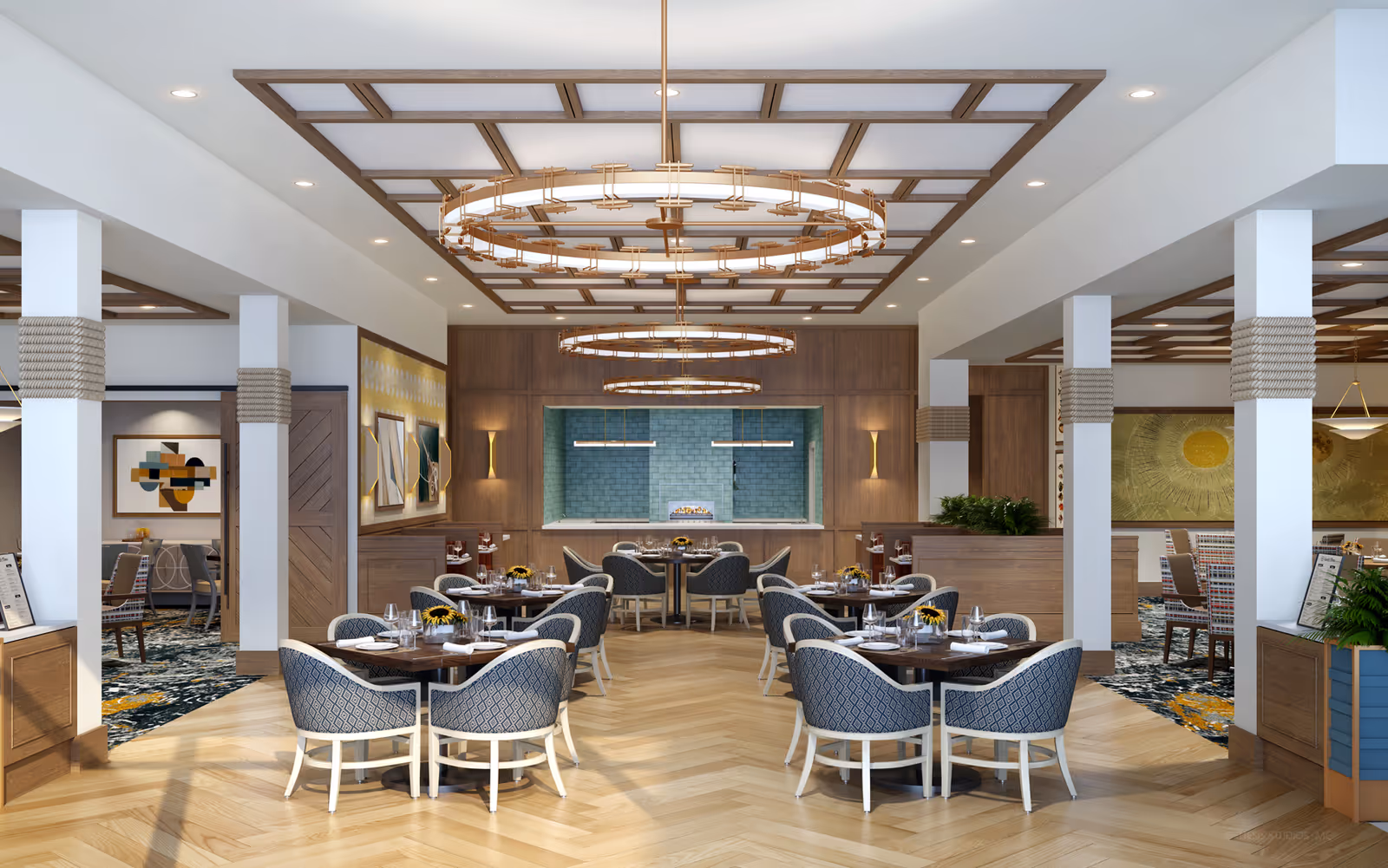 A spacious, well-lit dining room with wooden floors and modern circular chandeliers hanging from a coffered ceiling. The room features multiple tables with blue patterned chairs, set with plates, glasses, and napkins. The back wall has a teal tiled area with a fireplace and two pendant lights. Decorative artwork and plants add to the inviting atmosphere.