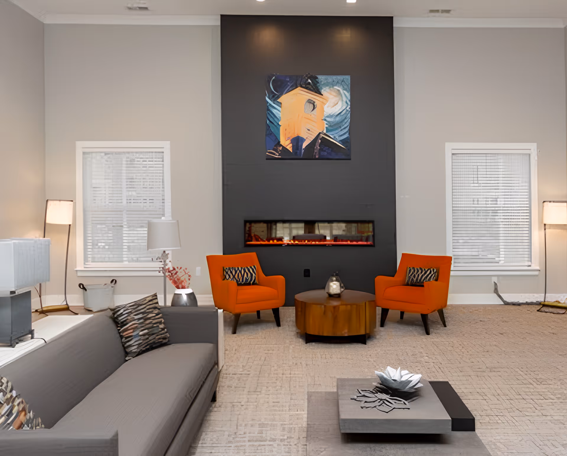 Contemporary lounge with a gray sofa, two orange armchairs facing a recessed electric fireplace and artwork on a dark accent wall.