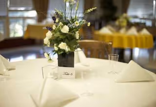 A round dining table with a floral centerpiece and folded napkins in a banquet hall.