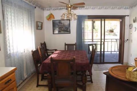 Dining room with red tablecloth, wooden chairs, and sliding glass door to a balcony.