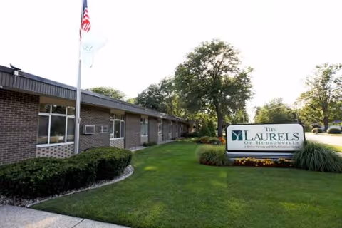 Front exterior of Laurels of Hudsonville senior living facility with sign and landscaping.